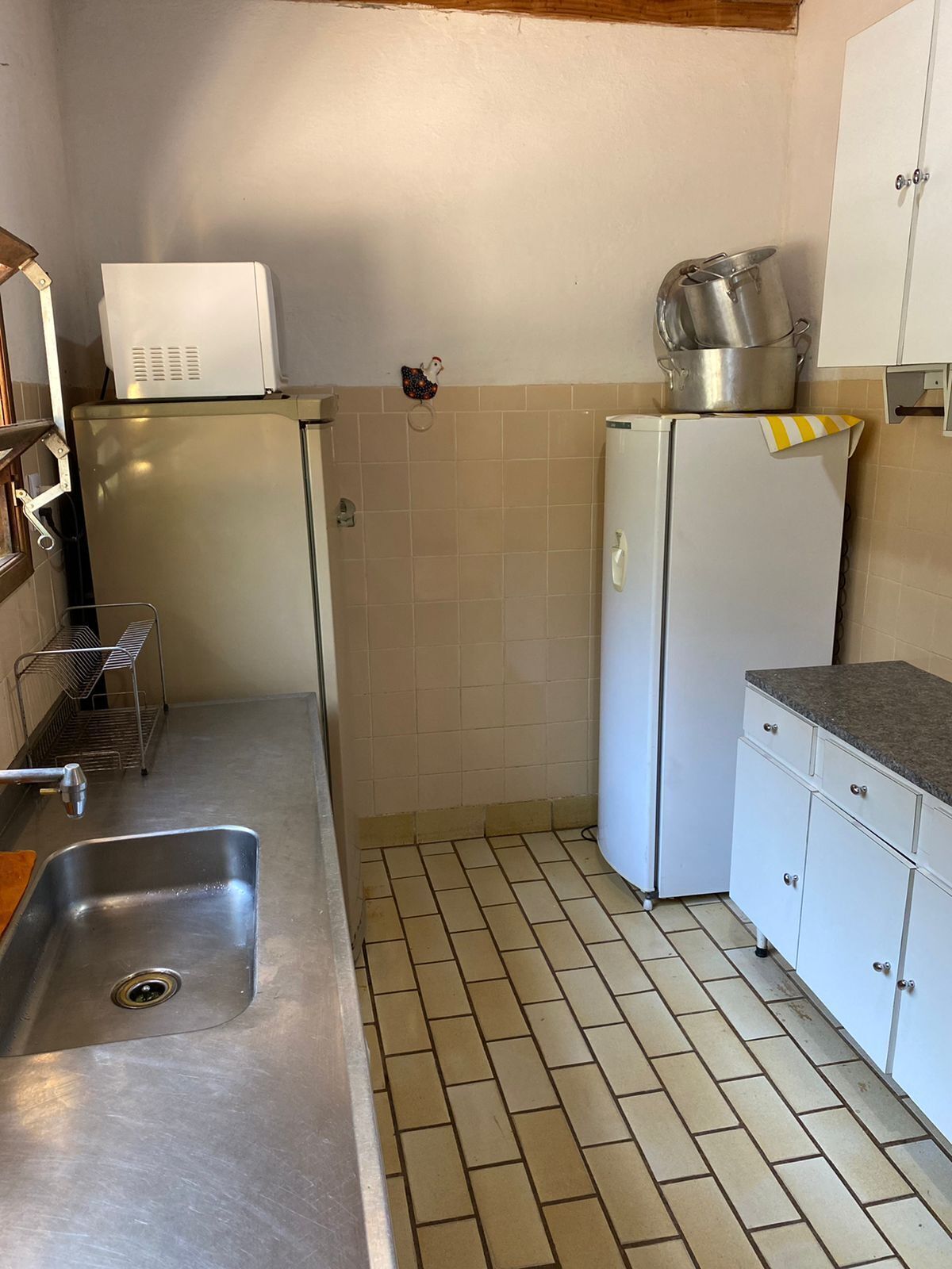 A compact kitchen with a sink, a microwave, a refrigerator, and a small shelf.