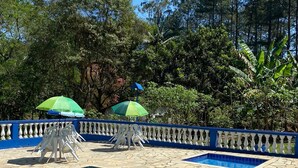 A swimming pool with clear blue water, surrounded by a white balustrade and stone tiles. There are two green umbrellas providing shade. - Property with swimming pool, soccer field, Wi-Fi, and a lake with many fish. (Igaratá)