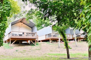 A row of treehouse-style cabins with wooden decks and enclosed seating areas, surrounded by trees.