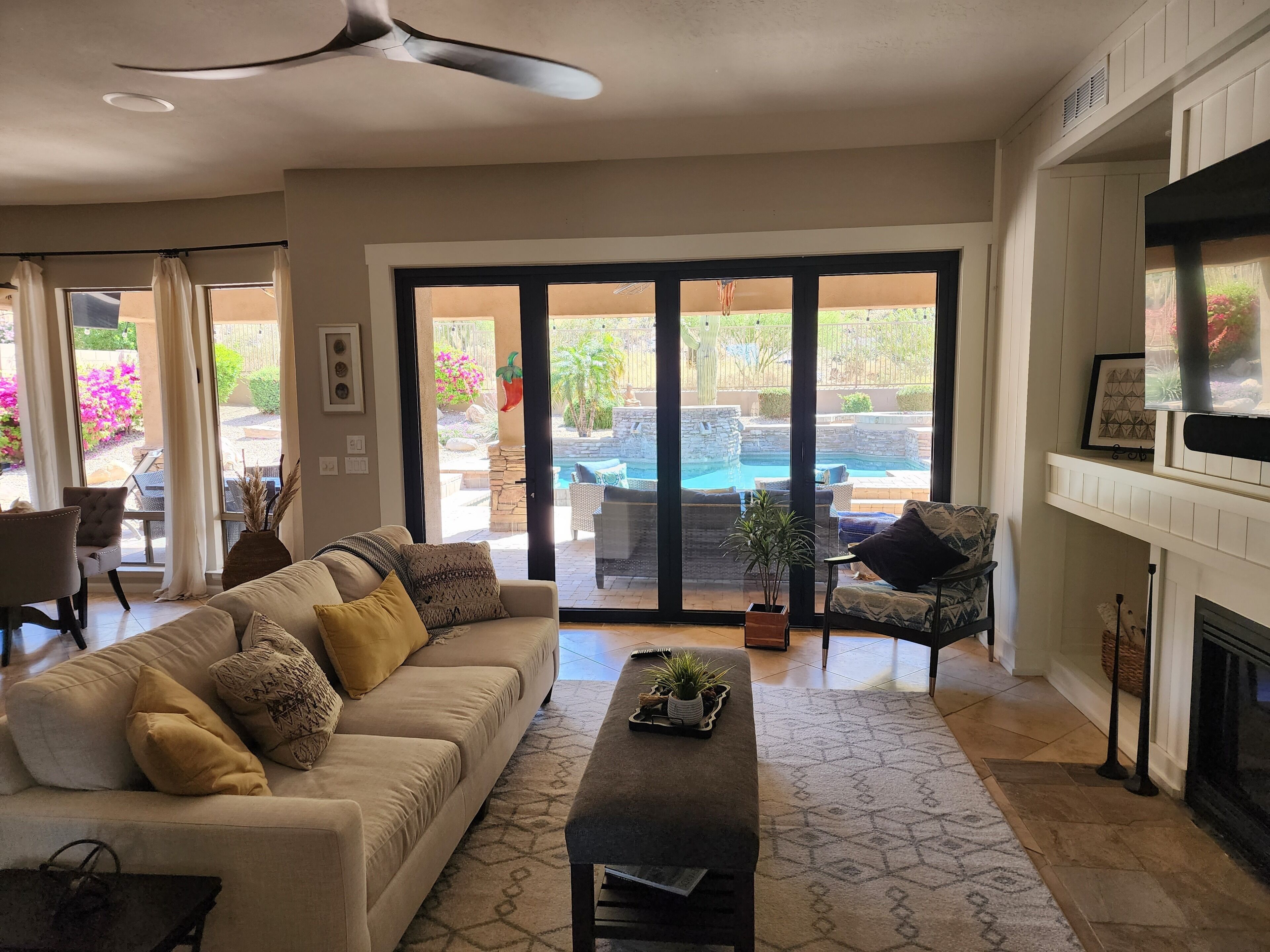 A spacious living room with a large sofa, a coffee table, and a fireplace. There is a sliding glass door leading to an outdoor patio with a pool.