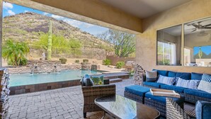 Une terrasse couverte avec une piscine, du mobilier d’extérieur et une vue sur un paysage montagneux.
