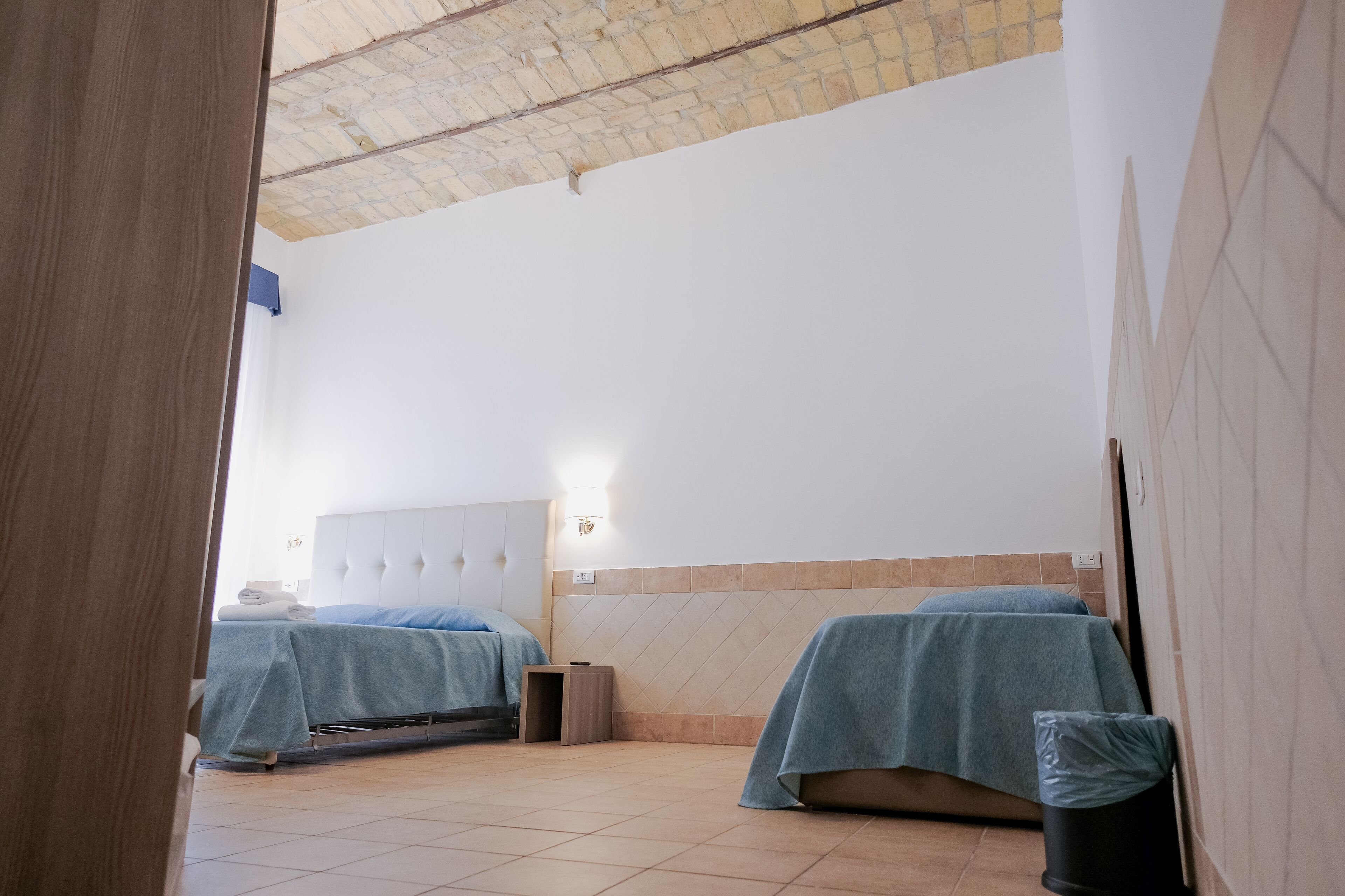 A hotel room with two beds, a tiled floor, and a brick ceiling.