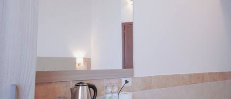 A hotel room with a wooden counter, a kettle, glasses, and toiletries.