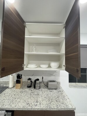 A kitchen with wooden cabinets, a granite countertop, and white shelves.