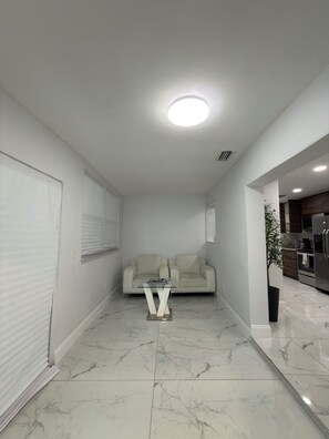 A modern living room with a sofa, a glass coffee table, and a kitchen in the background.