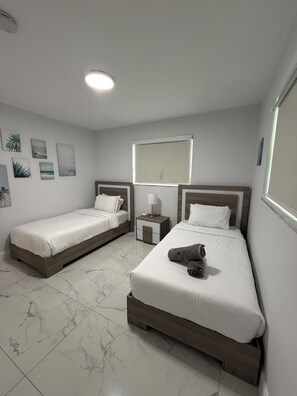 Une chambre d’hôtel avec deux lits, une table de chevet, une lampe et un luminaire au plafond.