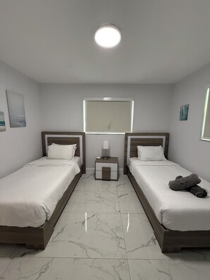 A hotel room with two single beds, a nightstand with a lamp, a large window, and a ceiling light. - Stylish, Comfortable 3 bedroom house (Hallandale Beach)