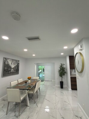 Un espace repas moderne avec une table en verre, des chaises blanches et un tableau accroché au mur.