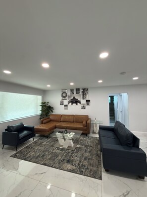 A modern living room with a sectional sofa, a glass coffee table, and a large window. - Stylish, Comfortable 3 bedroom house (Hallandale Beach)