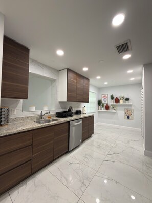 A modern kitchen with a dishwasher, marble countertops, wooden cabinets, and recessed ceiling lights.