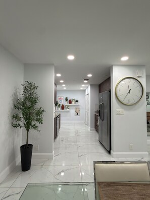 Une cuisine moderne avec un sol en marbre, une plante en pot et une horloge murale.