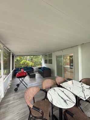 Un espace extérieur abrité comprenant un barbecue, des sièges et une table.