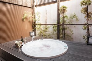 Ein Whirlpool mit Holzterrasse, umgeben von Bambuspflanzen, und eine Flasche Champagner.