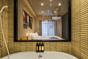 Ein modernes Badezimmer mit einer großzügigen Badewanne, einem Spiegel, der einen Schlafbereich reflektiert, und drei Toilettenartikeln an der Wand.