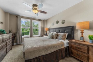 Un dormitorio con cama, ventilador de techo, mesita de noche, cómoda y ventana con cortinas.
