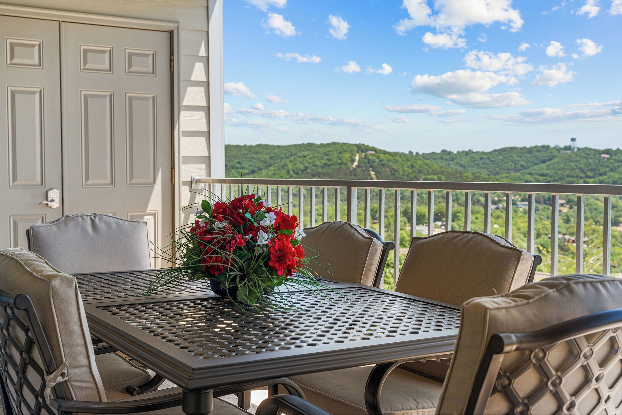 A balcony with a table and chairs, a door, and a view of a green landscape.
