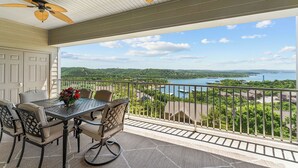 Een balkon met een tafel en stoelen, een plafondventilator en uitzicht op een meer en het omliggende landschap.