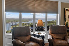 A room with two leather chairs, a table with a lamp, and a view of a lake through large windows. - Luxury & Spacious Condo with Fantastic Lake Views Near Silver Dollar City w Free Tickets (Branson)