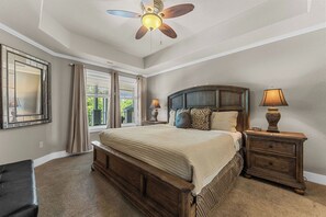 Une chambre à coucher avec un grand lit, deux tables de chevet, un ventilateur de plafond et une fenêtre avec des rideaux.