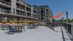 Een terras buiten met tafels en stoelen, omgeven door een hek en een rood zonnescherm.