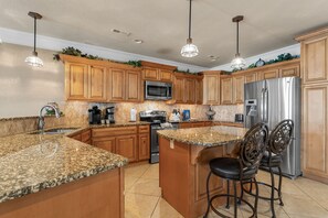 A kitchen with wooden cabinets, granite countertops, stainless steel appliances, and pendant lighting.