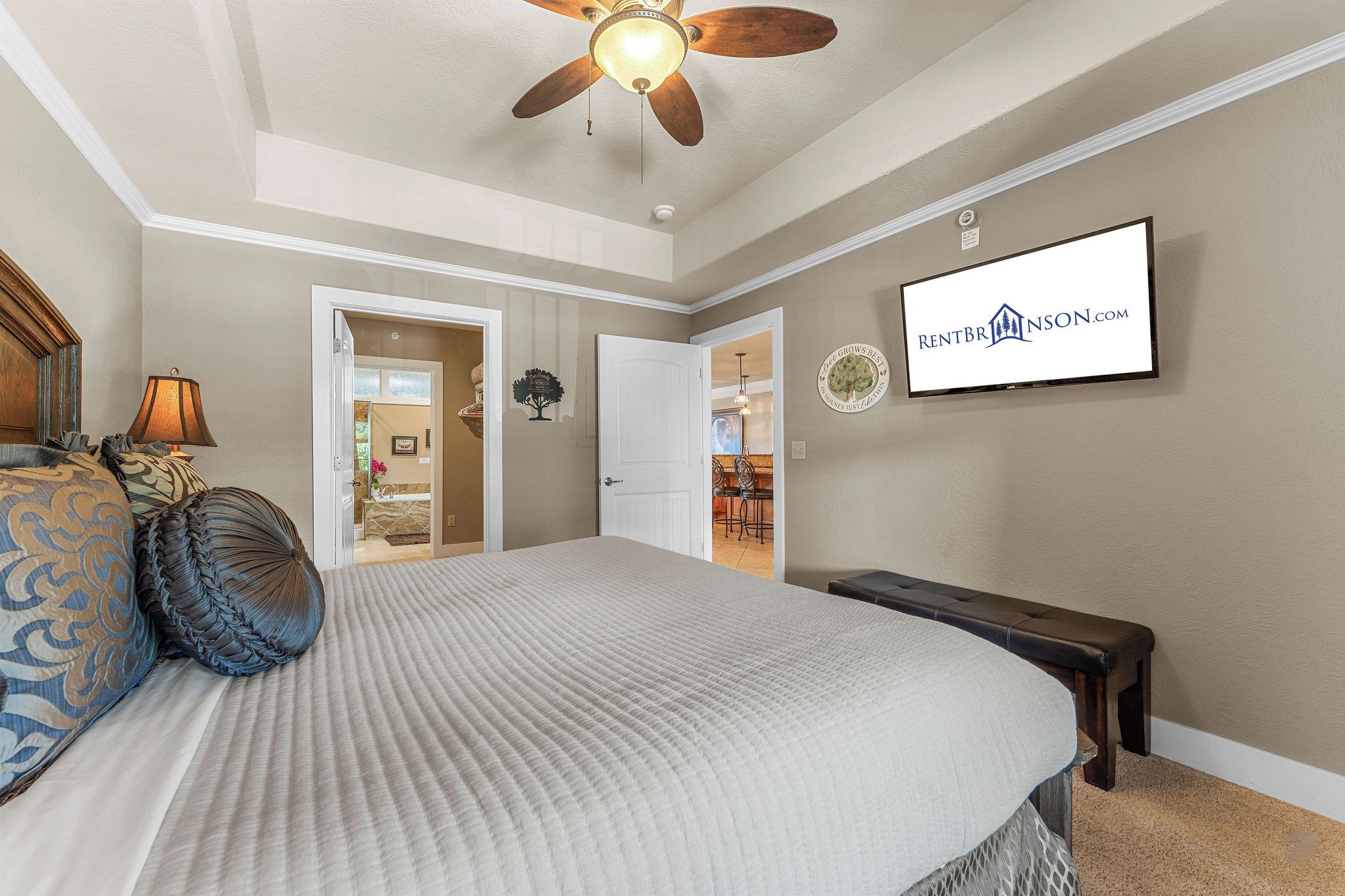 A bedroom with a bed, a ceiling fan, a TV, and a door leading to a bathroom.