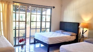 A hotel room with a large sliding glass door leading to an outdoor area, a bed with a dark headboard, and a bedside lamp. - La Maison Bleue (Cancun)