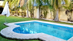 A rectangular swimming pool with a curved edge, surrounded by a grassy lawn and palm trees. - La Maison Bleue (Cancun)
