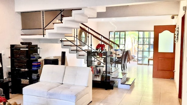 A spacious living room with a white sofa, a staircase, and a view of the outdoors. - La Maison Bleue (Cancun)