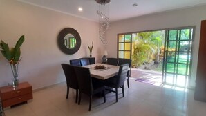A dining area with a table and chairs, a mirror on the wall, and a view of greenery outside. - La Maison Bleue (Cancun)