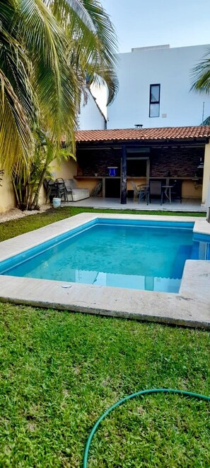 A swimming pool with a tiled deck, surrounded by grass and palm trees. - La Maison Bleue (Cancun)