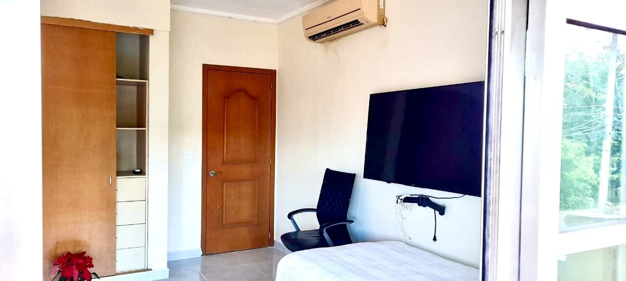 A bedroom with a bed, a chair, a wardrobe, and a TV mounted on the wall.