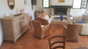 A living room with wicker furniture, a fireplace, and a television mounted on the wall. - Villa La Louvière- swimming pool, air conditioning, 7mn walk from the beach  (La Croix-Valmer)
