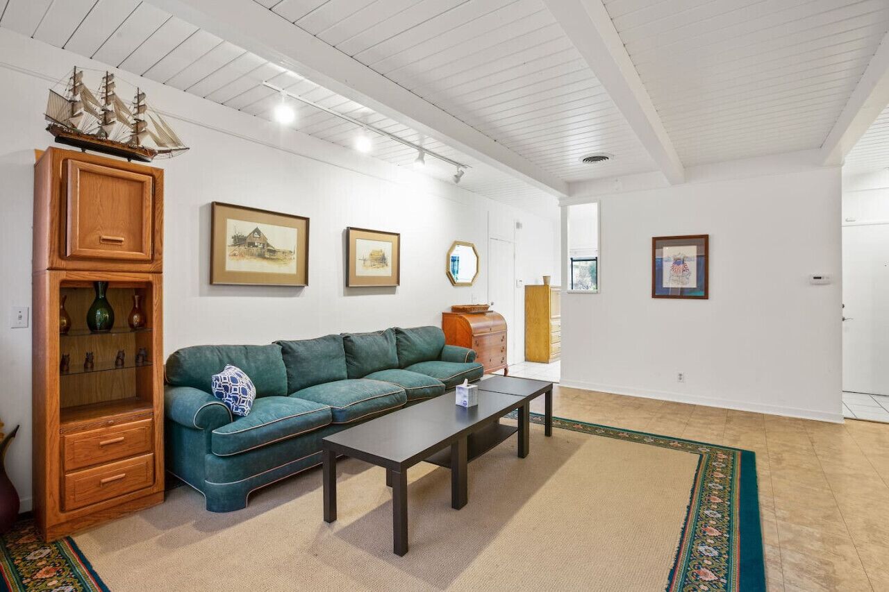 A spacious living room with a green sofa, wooden cabinet, and a ship model on the wall.