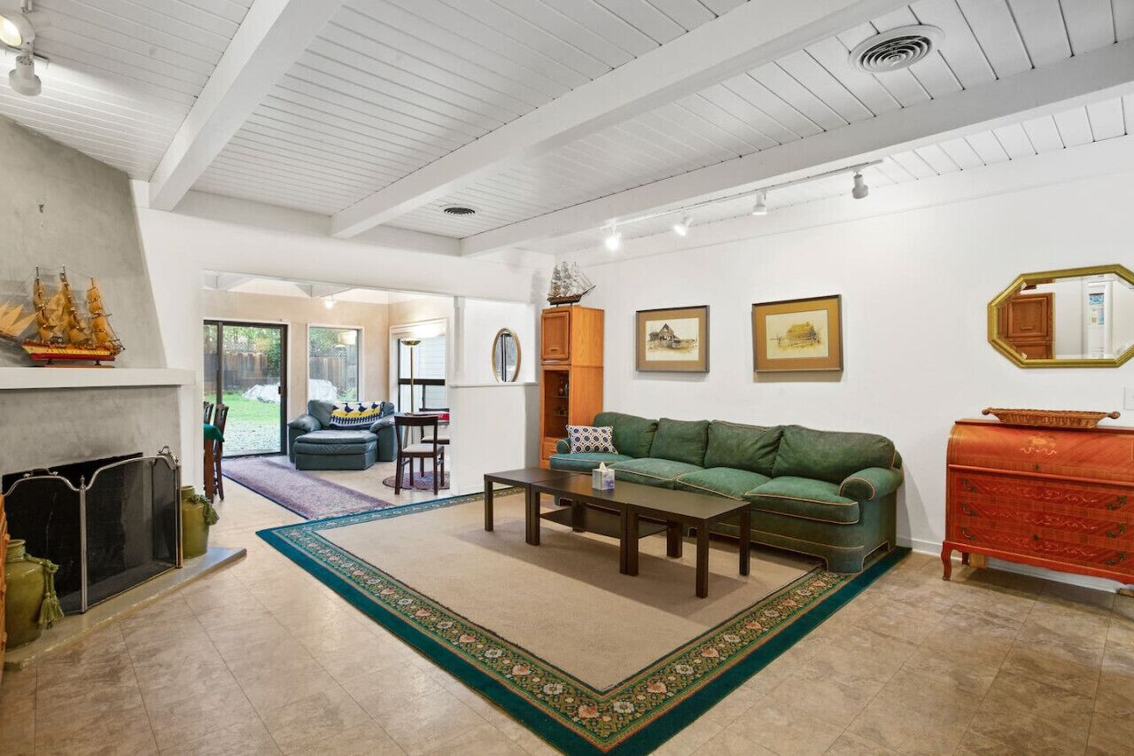 Un salón amplio con un sofá verde, una mesa de centro de madera y una chimenea. Hay cuadros enmarcados en la pared y un espejo grande sobre el tocador.