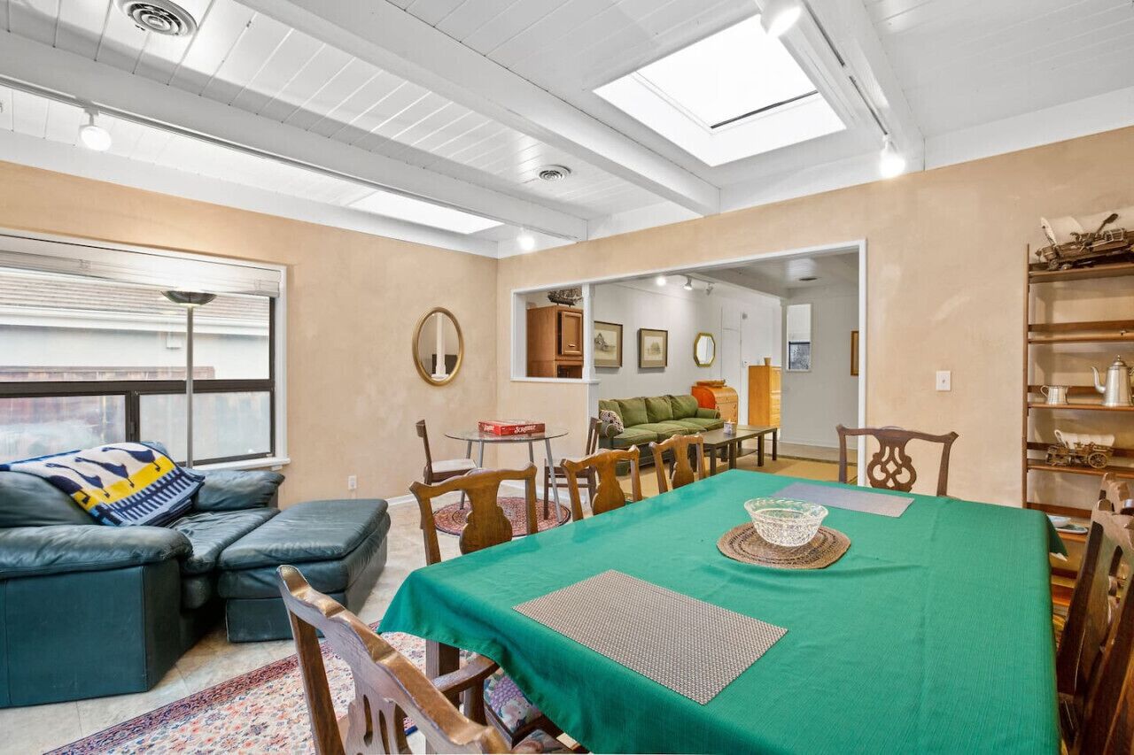 A dining area with a green tablecloth, wooden chairs, and a sofa with a patterned throw.