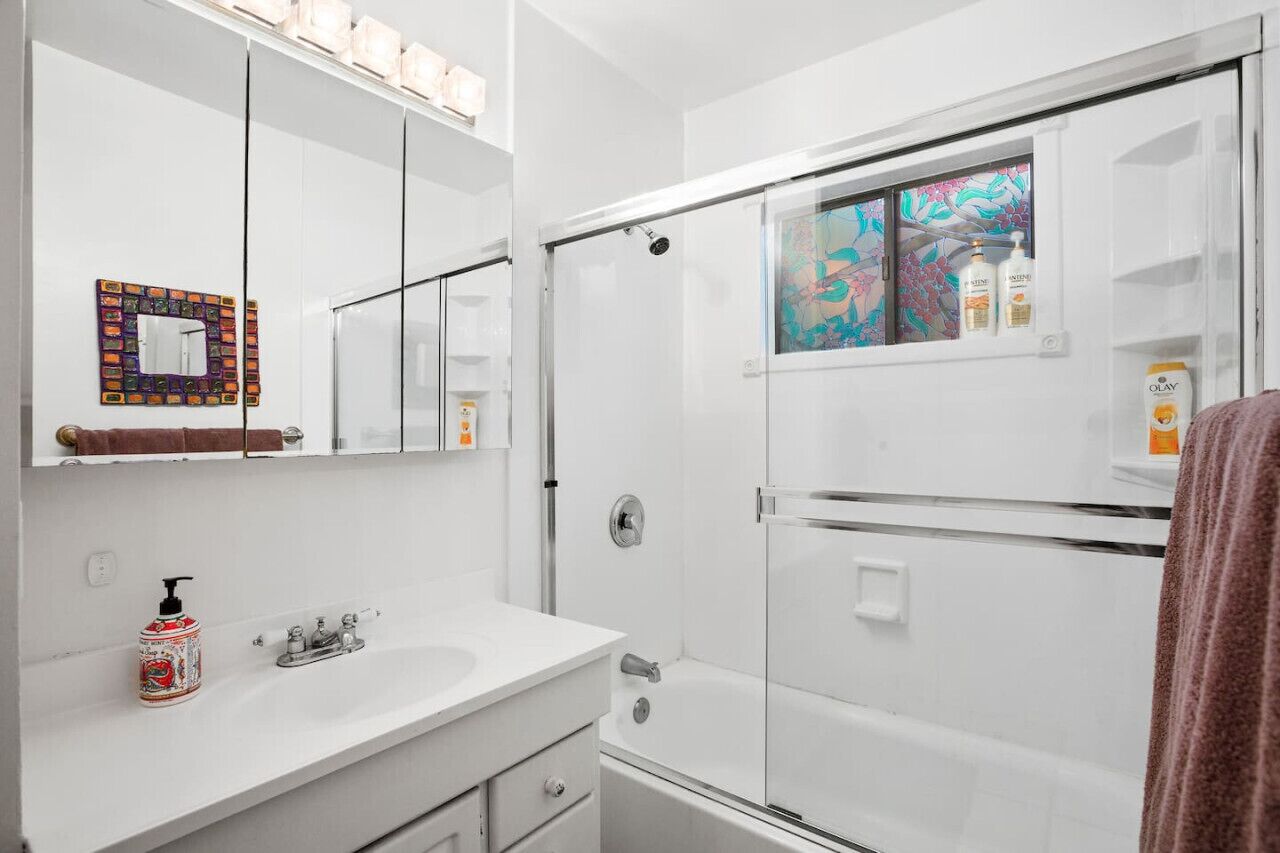 Un baño moderno con un lavamanos blanco, una cabina de ducha de vidrio y un espejo con un marco colorido.