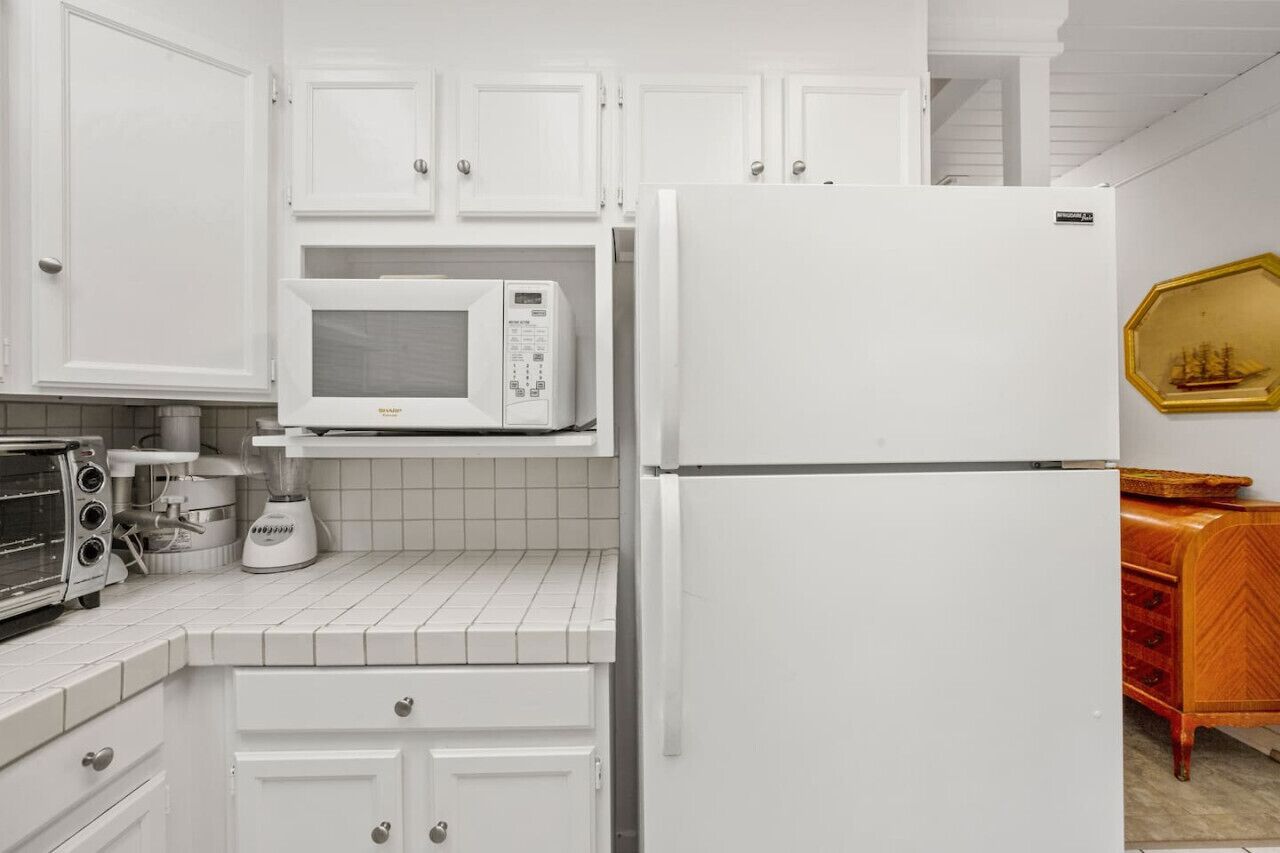 A kitchen with white cabinets, a white refrigerator, a microwave, a toaster, and a blender.