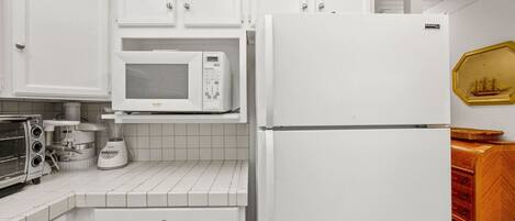 A kitchen with white cabinets, a white refrigerator, a microwave, a toaster, and a blender.