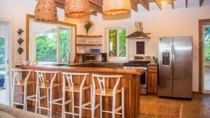 A modern kitchen with a central island, bar stools, hanging light fixtures, and a stainless steel refrigerator. - Sea Cloud, Private home with salt water pool / Sea views (West Bay)