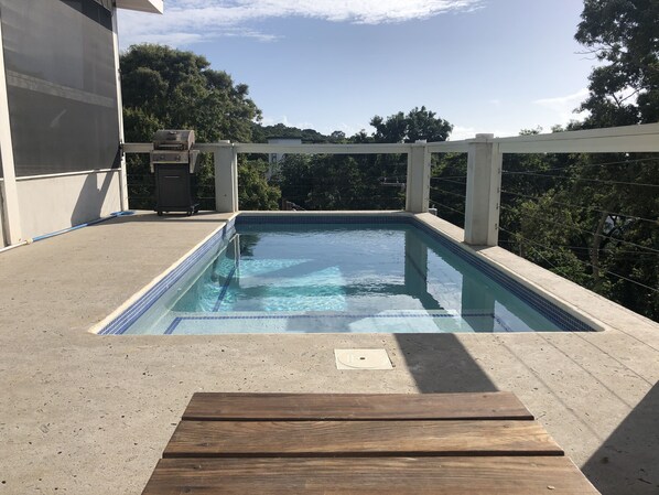 A rectangular outdoor pool with clear blue water, surrounded by a concrete deck and a wooden bench. - Sea Cloud, Private home with salt water pool / Sea views (West Bay)