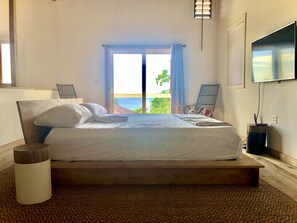 Un dormitorio con cama de madera, vista al mar, televisión y una silla junto a la ventana.