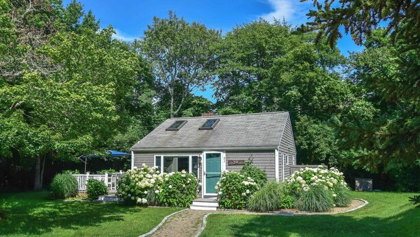 A small house with a sloped roof, a front door, and a pathway leading to the entrance.