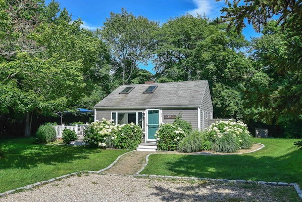 A small house with a sloped roof, a front door, and a pathway leading to the entrance.