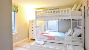 A bunk bed with a window, a dresser, and a small table.