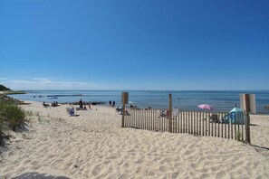 A sandy beach with a wooden fence, beach chairs, and umbrellas.