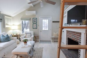 A cozy living room with a white sofa, a coffee table with a plant, a fireplace, and a TV.