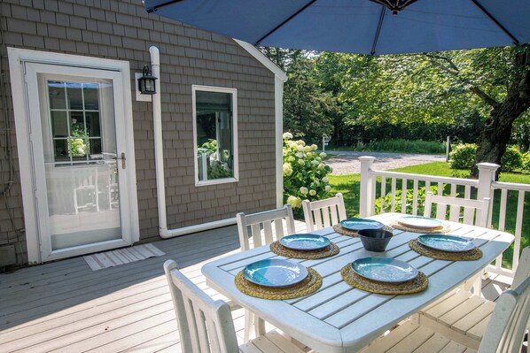 A covered patio with a table set for dining, a white fence, and a garden view.