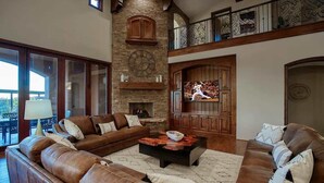 A spacious living room with a large leather sectional sofa, a fireplace, and a television.