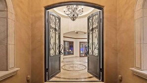 A grand entrance with a chandelier, a circular patterned floor, and a view into a spacious interior.